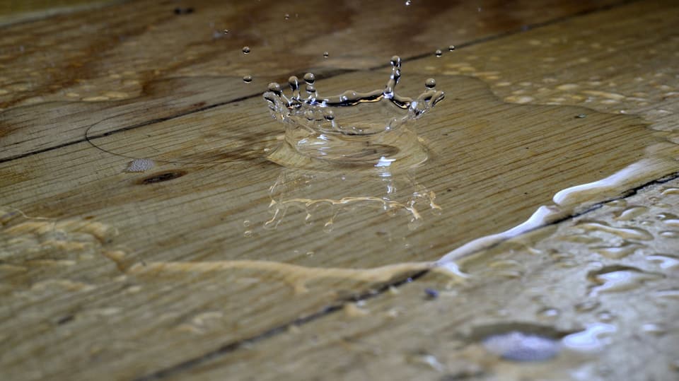A drop splashing into a puddle of water on a wooden plank floor