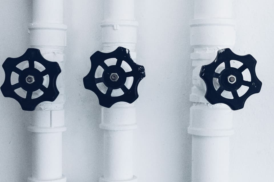 Three black valve handles on white-painted water pipes